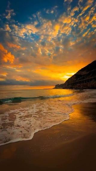 Golden sunlight dances on the blue ocean, with soft sand beneath and blue clouds above—a perfect moment in nature's paradise